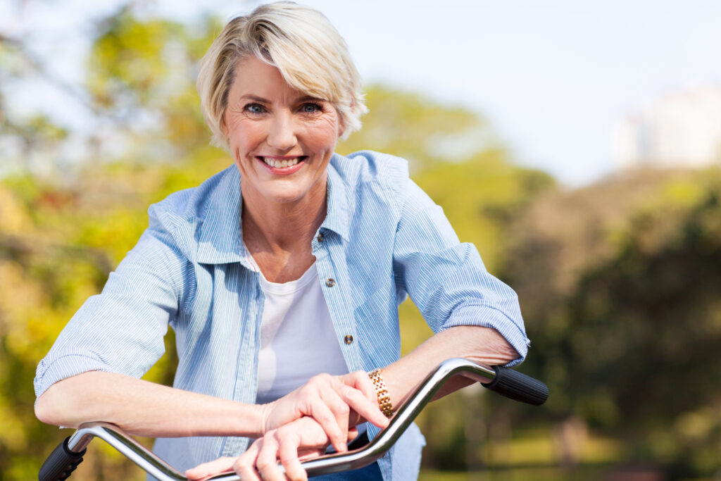 Older woman Leaning on the handle bars of a bike, smiling. Contact Us at Bayswater Dental Surgery.