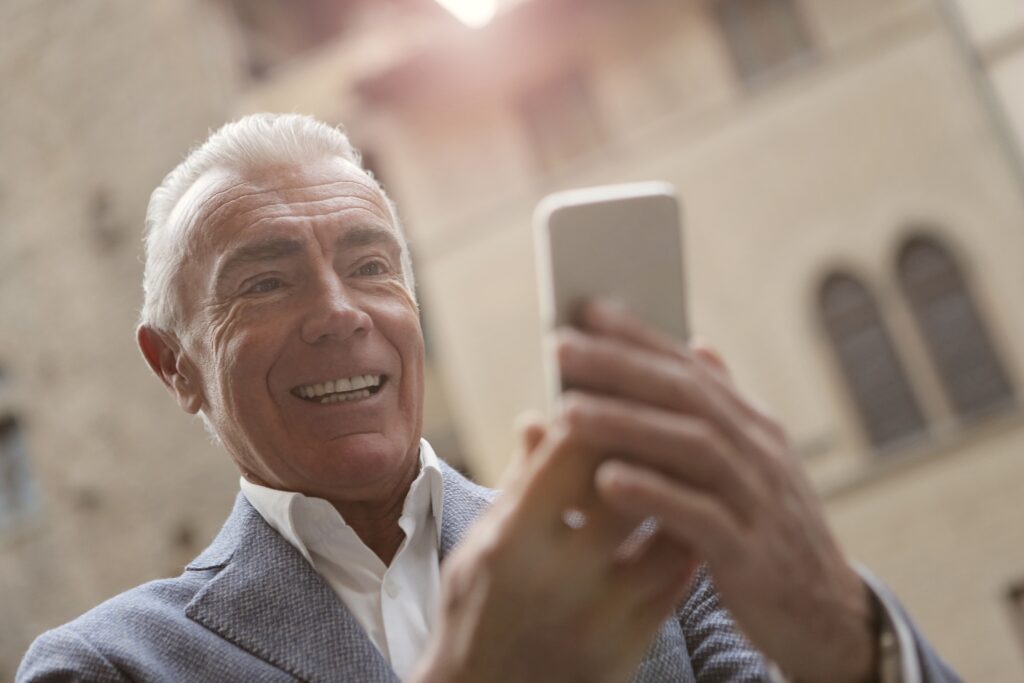 Older man smiling at phone searching for dentures near me. Dentures in Bayswater.